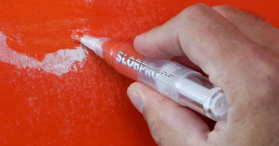 A person holding a Slobproof Paint Touch-Up Pen and painting an orange wall