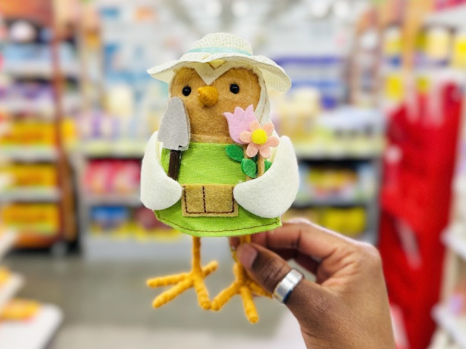 hand holding up a felt bird in a gardener outfit with flowers