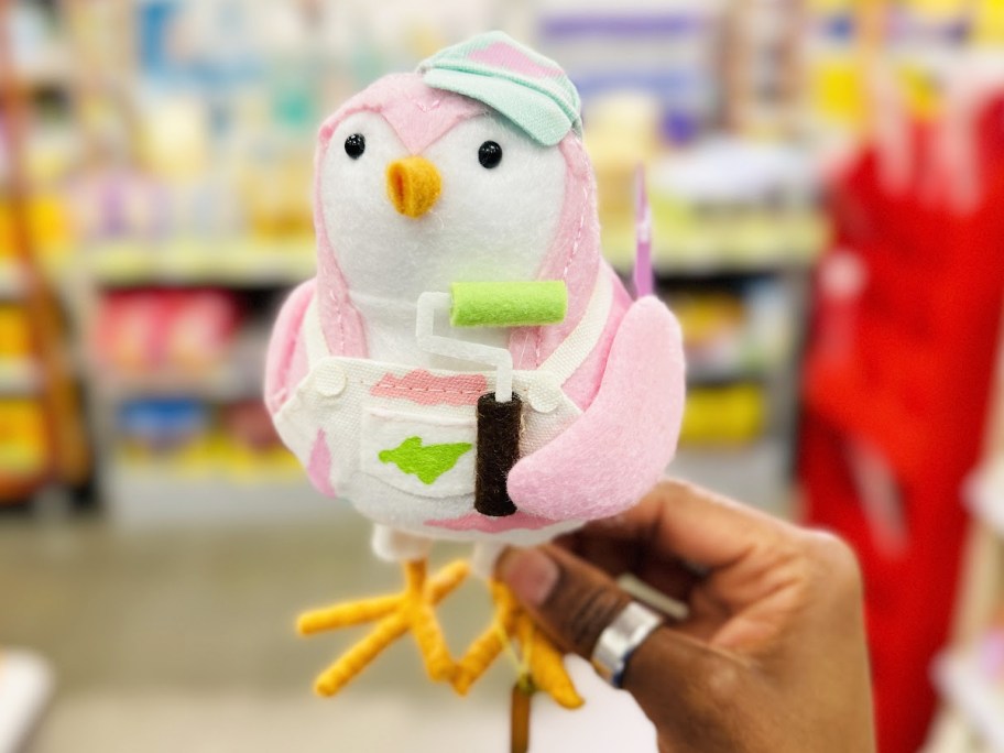 hand holding up a pink bird in a painters outfit