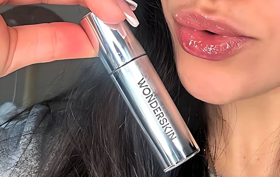 a woman holding a tube of lip oil next to her lips