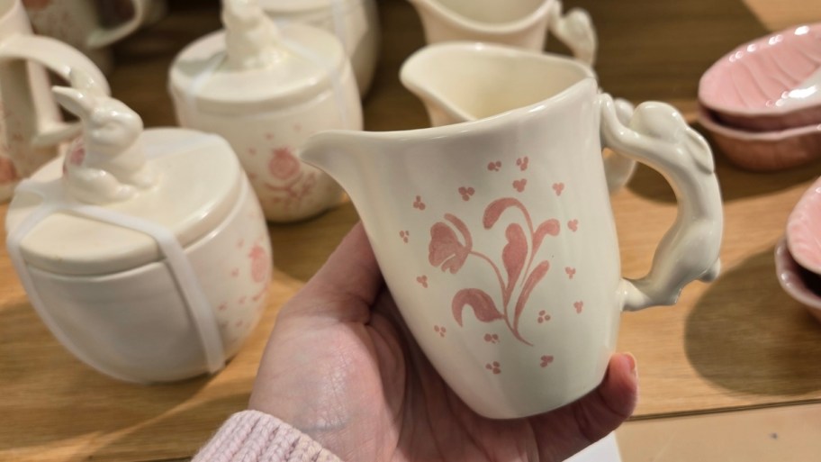 womans hand holding a hand painted cream pitcher