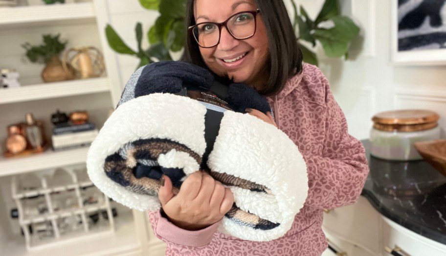 smiling woman holding a cuddl duds sherpa throw blanket in her living room