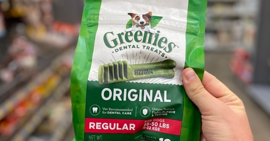 a womans hand holding a bag of greenies