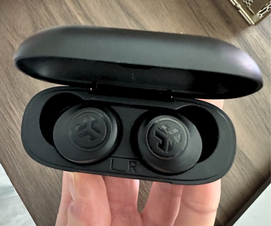 a man's hand holding a set of earbuds in a charging case