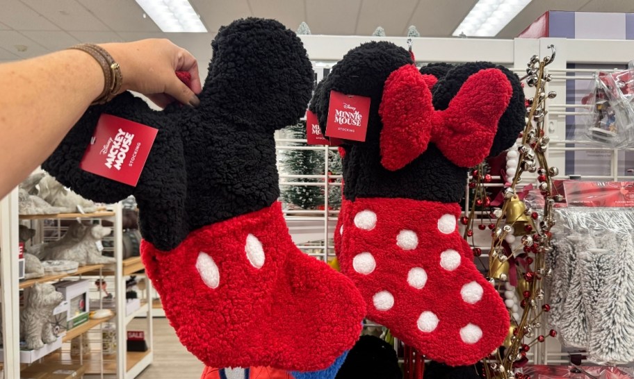 a womans hand holding a mickey mouse christmas stocking next to a minnie mouse version