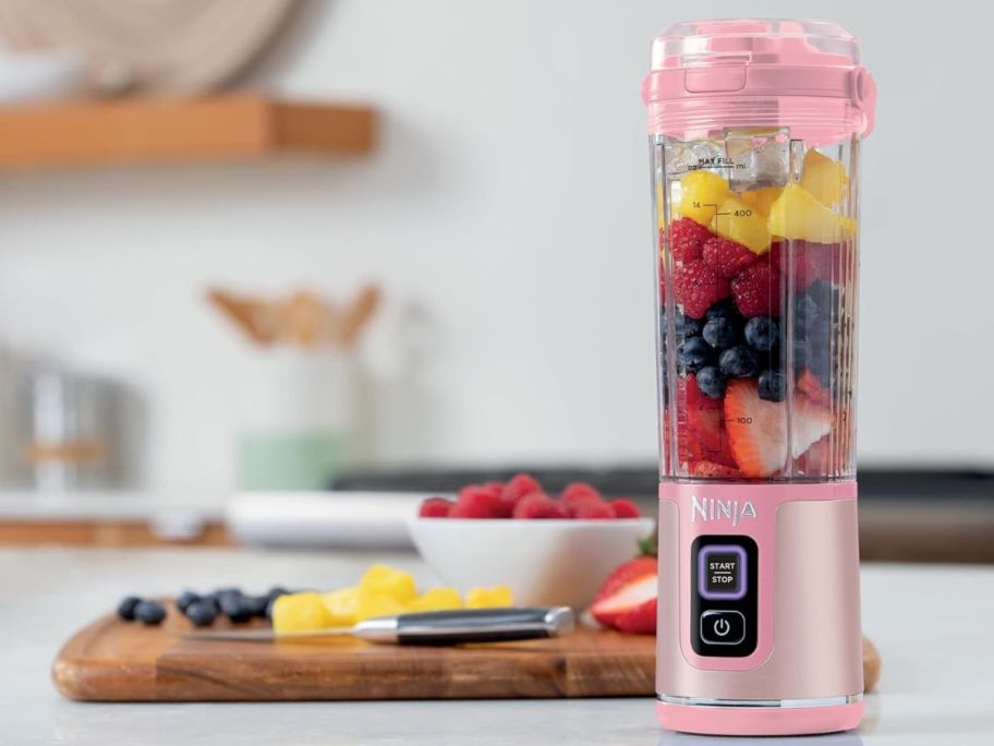 ninja blender with fruits next to a cutting board with fruit on it 