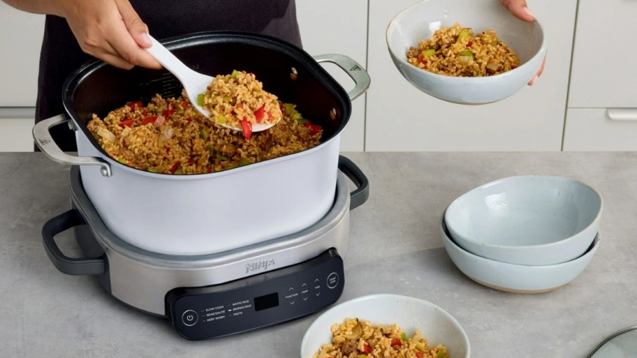 a person hands shown serving jambalaya from a ninja possible cooker