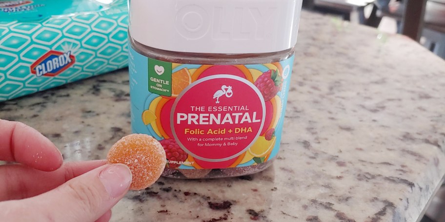 olly prenatal vitamins bottle on table with hand holding gummie