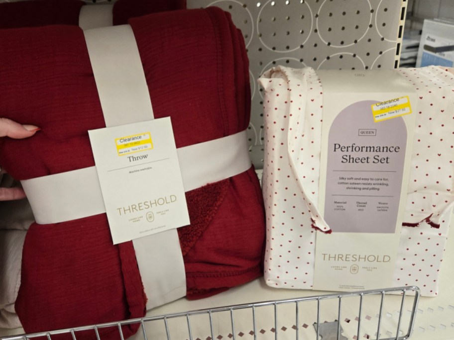 A red Threshold throw and a white Queen Performance Sheet Set with red dots, both on clearance. Displayed on a shelf with a perforated backdrop.