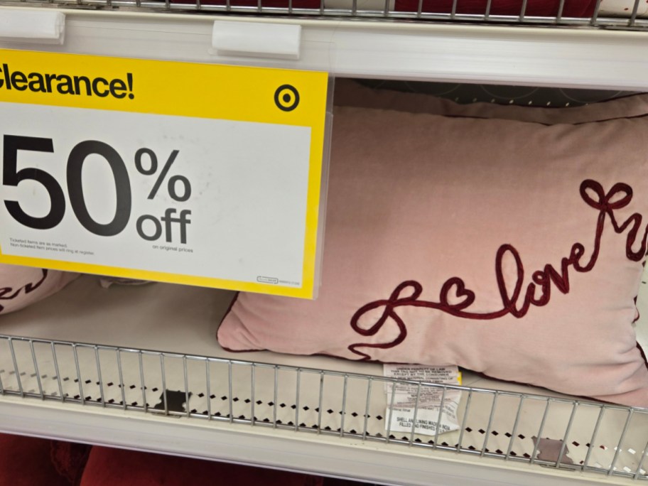 Clearance sale at a store featuring a pink pillow with "love" in red cursive. A yellow sign displays "50% off."