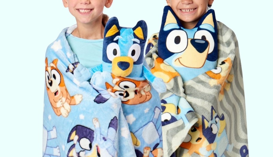 little kids wrapped in throw blankets and snuggling bluey plush toys