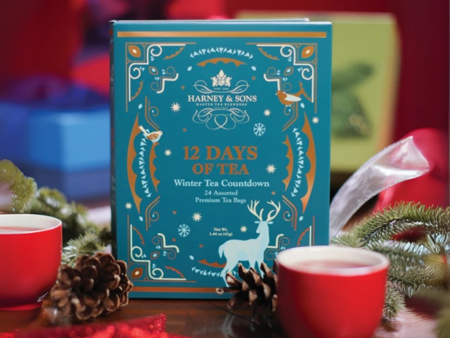 a Harney & Sons 12 Days of Tea Countdown Calendar box with cups of tea and holiday decor around it
