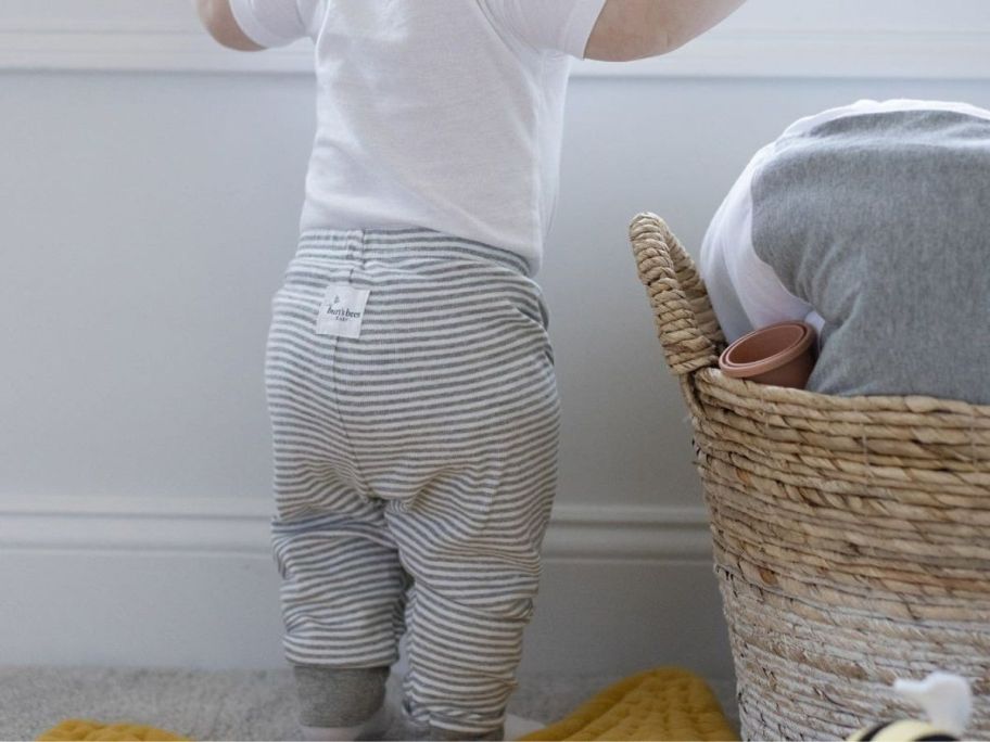 Burts bees baby boy standing up by the window wearing gray stripped pants