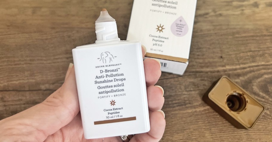 hand holding a white bottle of Drunk Elephant D-Bronzi Anti-Pollution Sunshine Drops