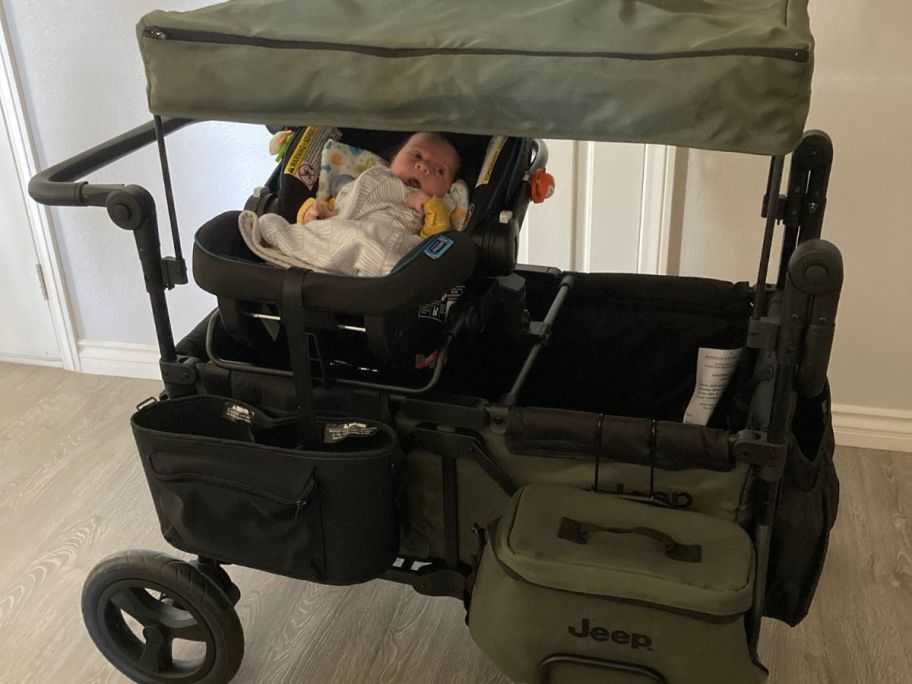 A jeep stroller wagon with a baby in a carseat inside