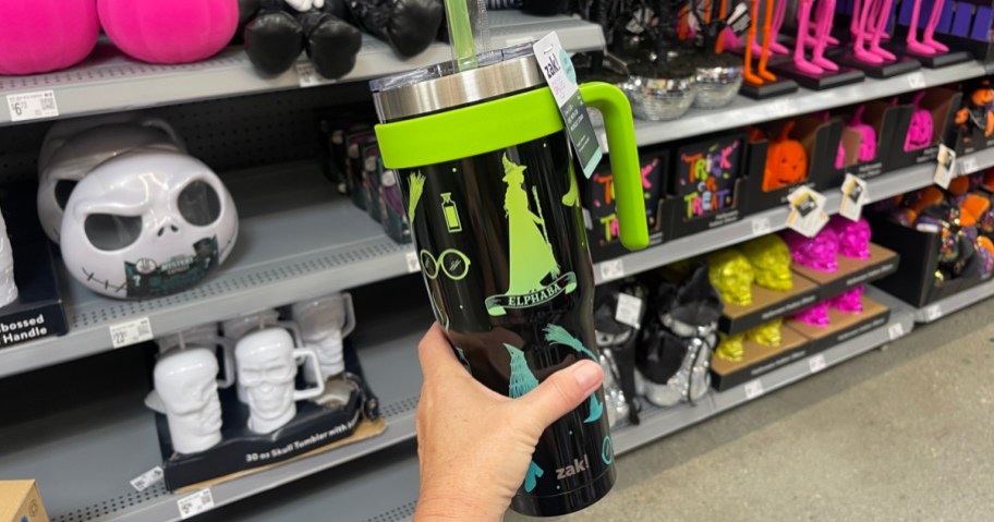 person holding up black and green Zak Elphaba Halloween Tumbler inside walmart store