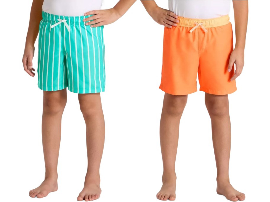 Two children wearing swim trunks stand side by side; one pair is turquoise with white stripes, the other is bright orange. Both have drawstrings.
