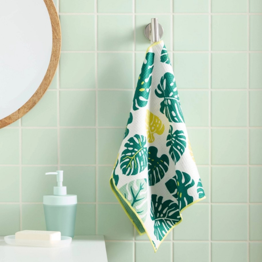 a reversible hand towel with monstera leaf print all over it, hanging next to a sink