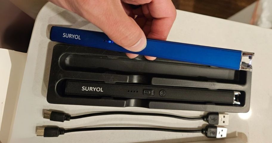 hand holding blue rechargeable lighter in hand above a black one and wires on table