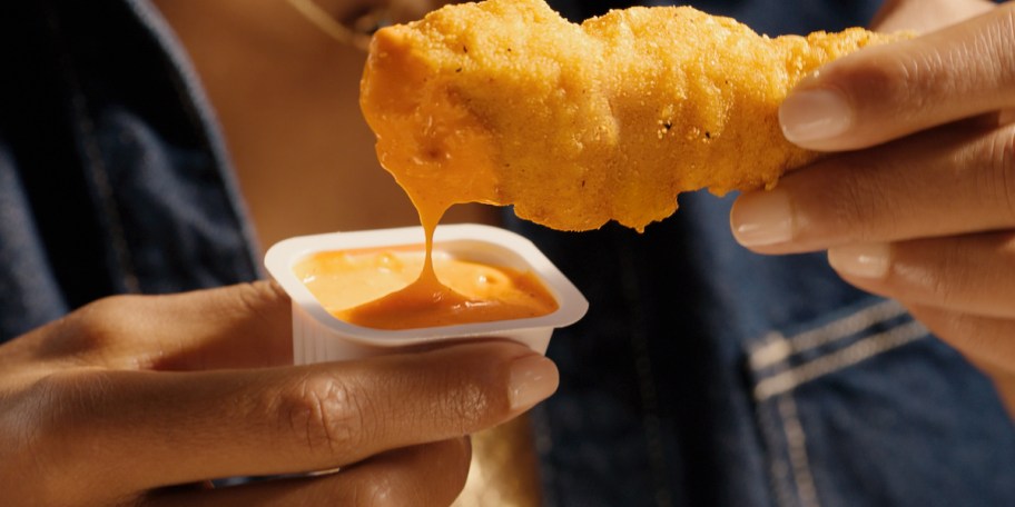 hand dipping chicken strip in sauce