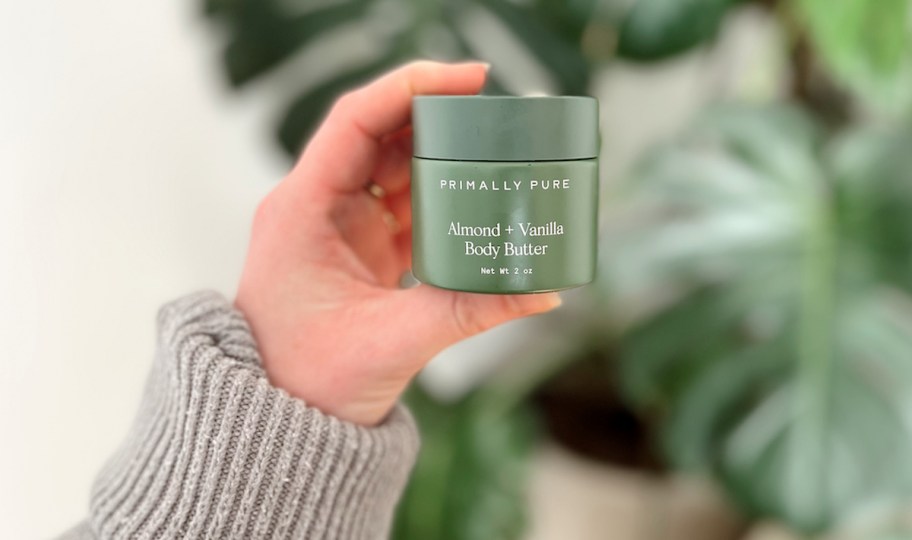 hand holding primally pure body butter in front of plant