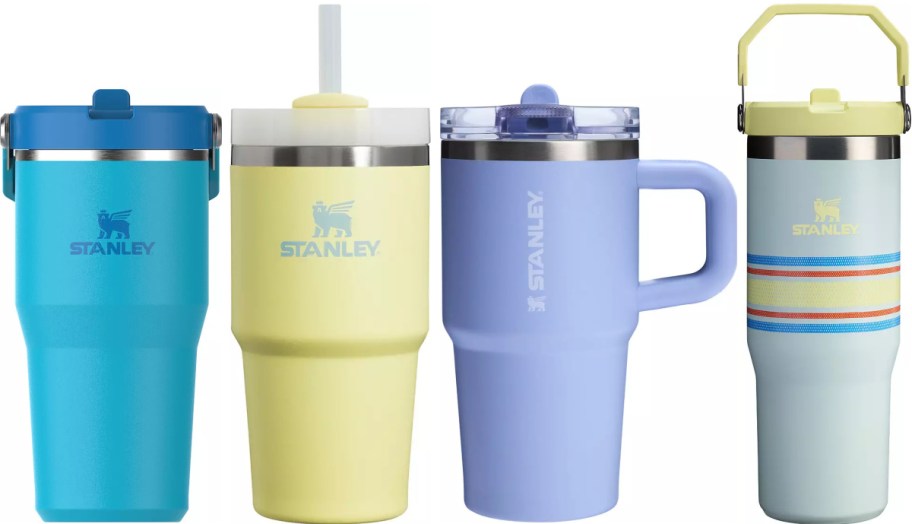 Four colorful Stanley tumblers are lined up. From left to right: blue with a flip lid, yellow with a straw lid, lavender with a handle, and light blue with stripes and a carrying handle.