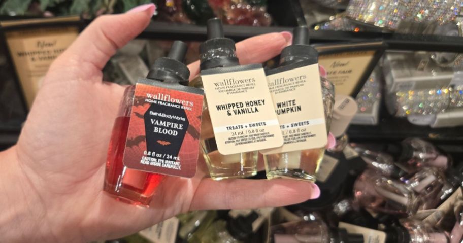 Hand holding 3 Bath & Body Works Wallflower Refills in Halloween & Fall Scents