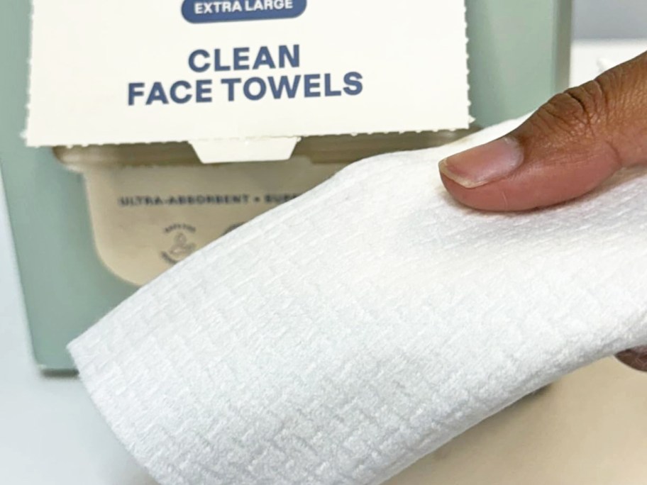 hand holding a face towel in front of a box of more