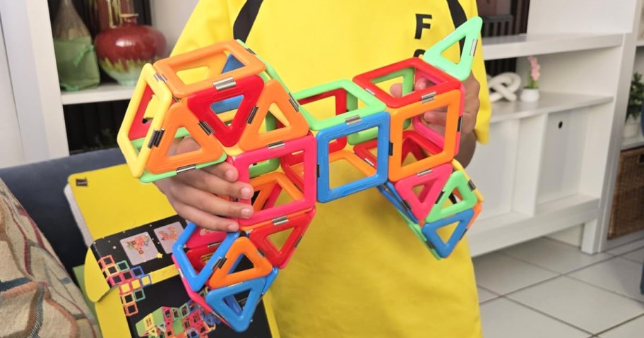 child holding up colorful creation made of magnetic tiles
