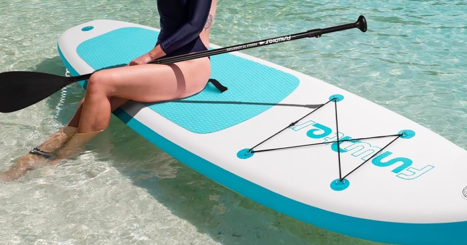 woman sitting on a white and blue paddle board in water