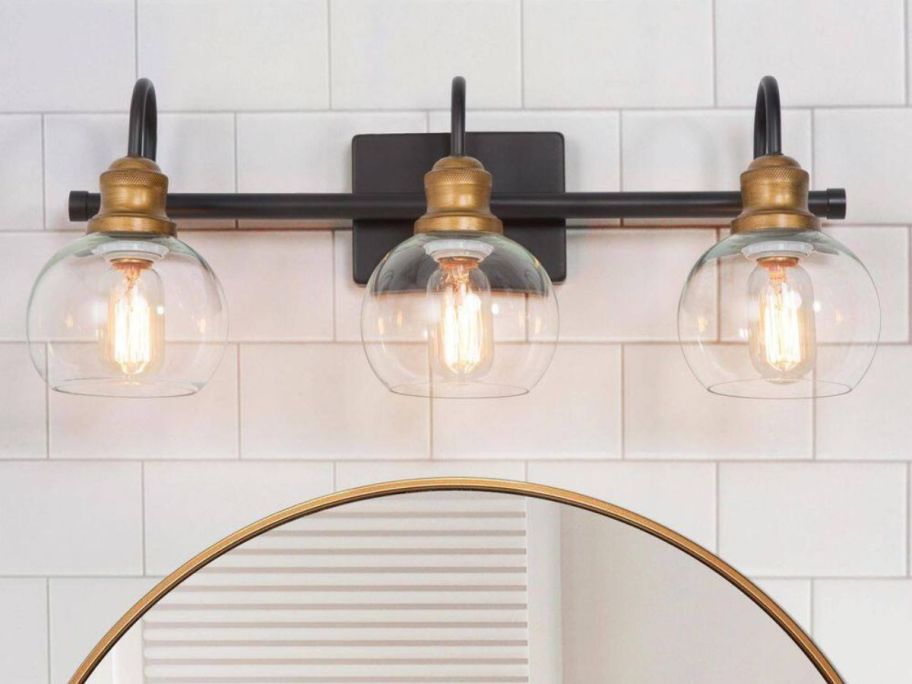 A LNC 22.5" 3-Light Modern Aged Brass & Black Vanity Light over a mirror