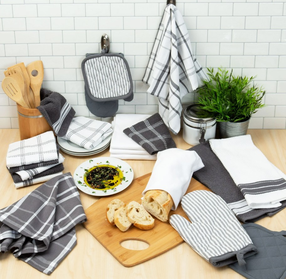 grey and white kitchen towels and pot holders on counter with cutting boards and loaf of bread