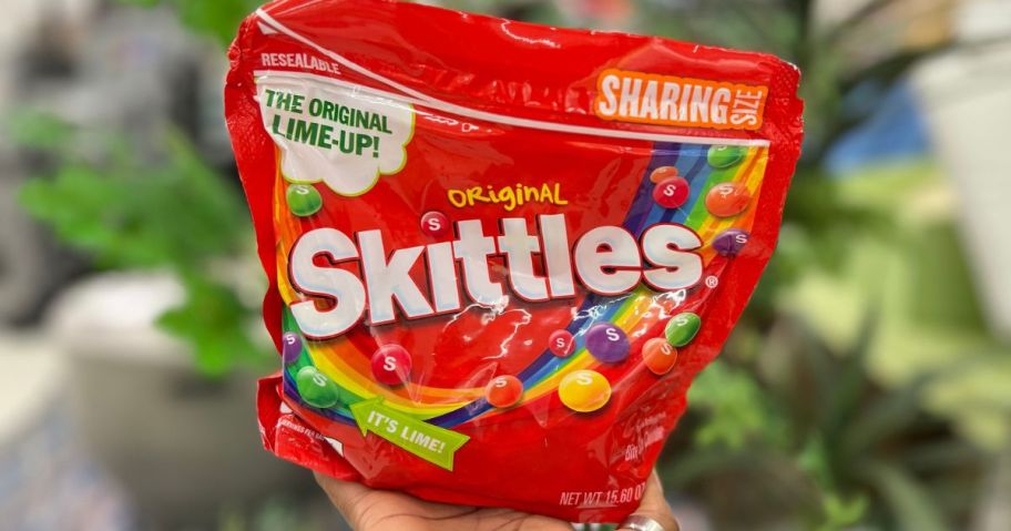 Hand holding a sharing size bag of Skittles