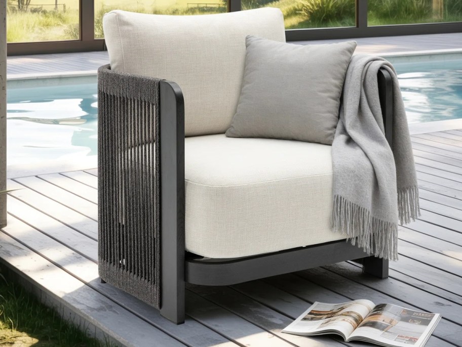 black rope chair with white cushions sitting next to in ground pool