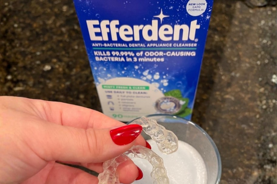 A person holding retainers near a box of Efferdent Cleaning Tablet 44-Count (Minty Fresh & Clean)