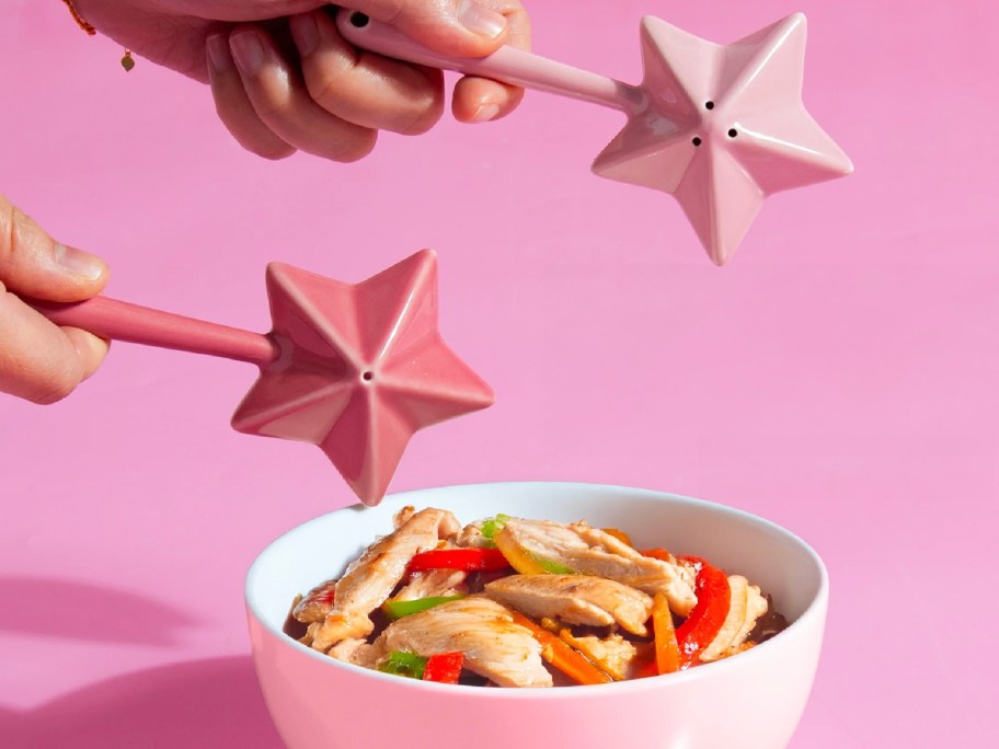 hands holding pink salt and pepper shakes over bowl of chicken