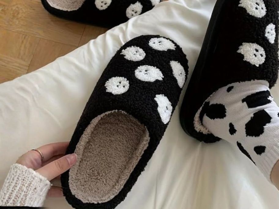 hand holding black and white halloween slipper with ghosts on it on bed