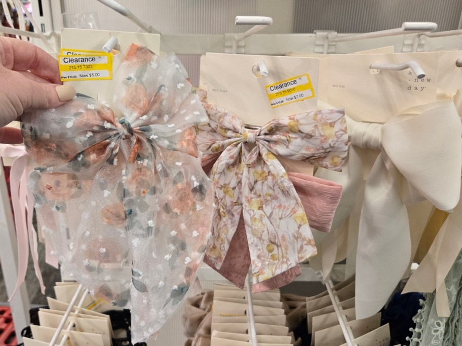 A display of floral hair bows on clearance, featuring pastel colors and delicate patterns. A hand holds a bow with a price tag of $5.00.