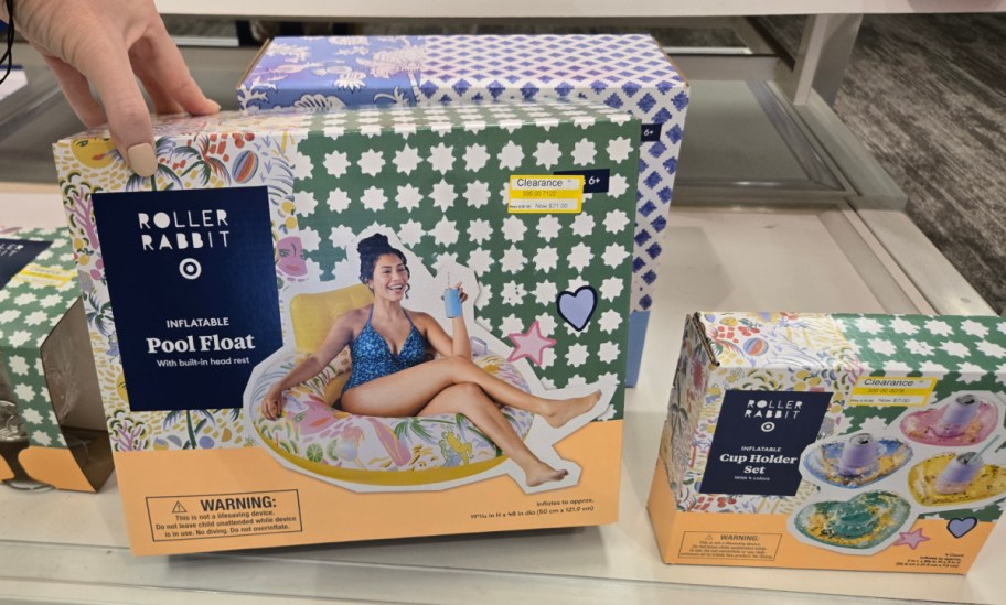 A box of a Roller Rabbit inflatable pool float with a smiling person lounging and holding a drink, displayed on a shelf.