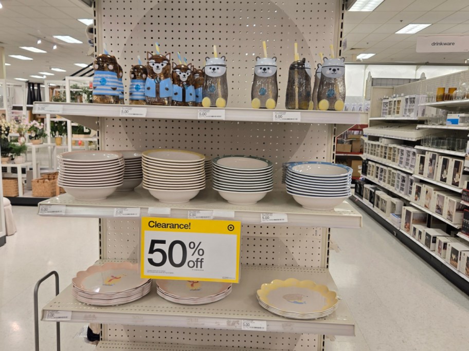 Store shelf displaying discounted tableware. Top shelf has cute bear-shaped bottles. Middle shelf has stacks of striped bowls. A "50% off Clearance" sign is prominent.