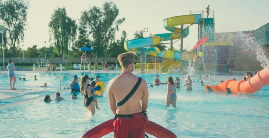 boy lifeguard standing in front of busy pool