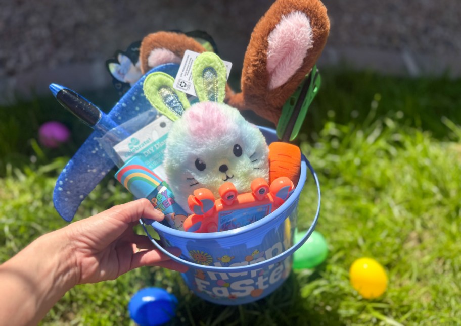 hand grabbing blue easter basket with brown bunny ears, bunny plush and more fillers