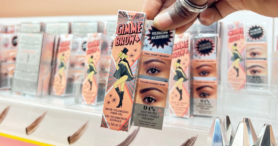 hand holding up a package of Benefit Cosmetics Gimme Brow in beauty store