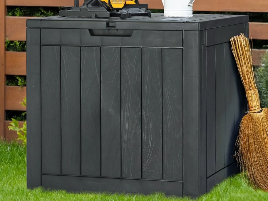 broom leaning up against a black deck box