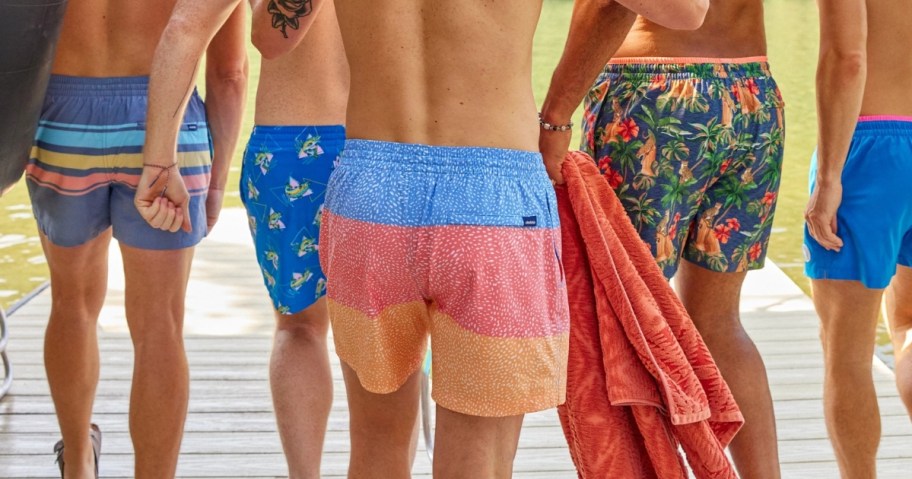 men walking with their backs to the camera, all are wearing colorful swim trunks
