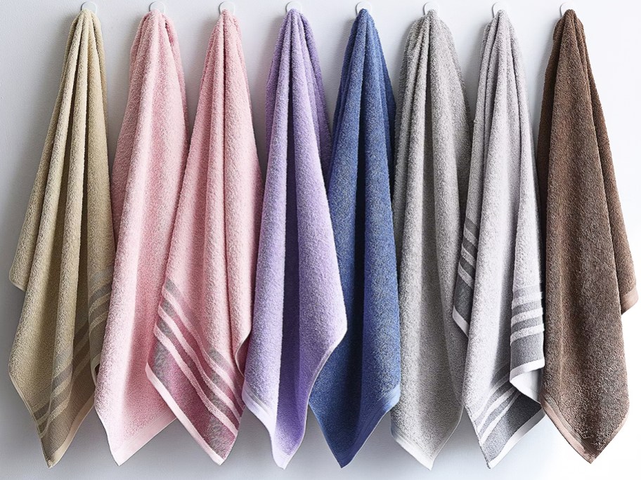multiple bath towels in various colors hanging on hooks on a wall