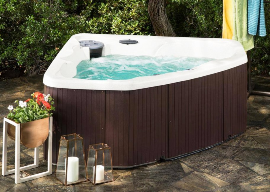 brown corner hot tub with candles and plants around it