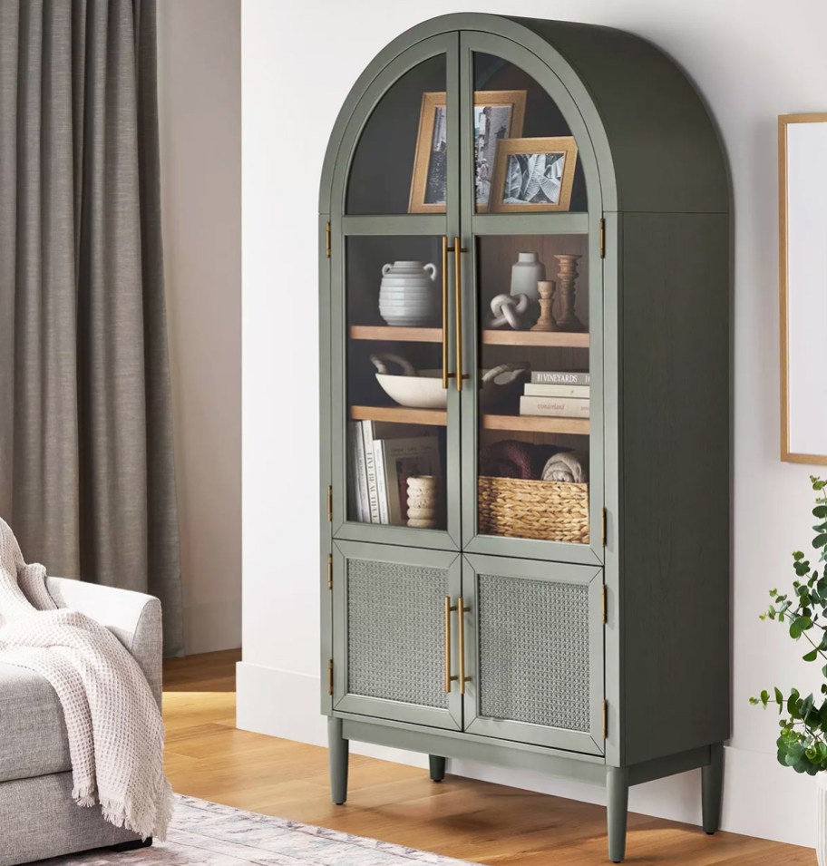 a green arched cabinet with glass doors and rattan bottom cabinet doors sitting in a living room