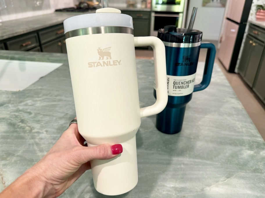 hand holding a white Stanley tumbler with a teal one in background