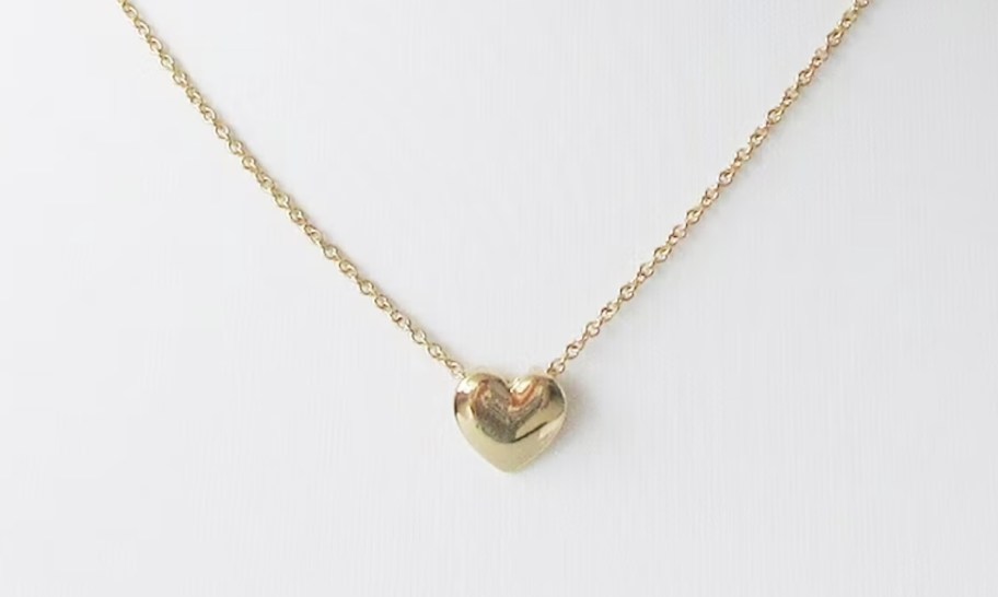 gold heart necklace on white stand